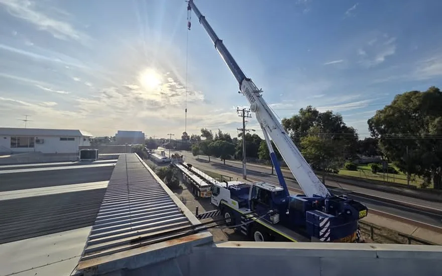 Mobile crane lifting roofing materials onto a commercial building at sunrise