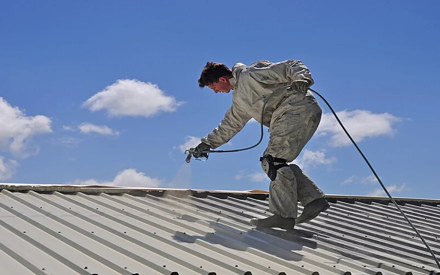 Painter spray coating a Colorbond roof alongside a restoration