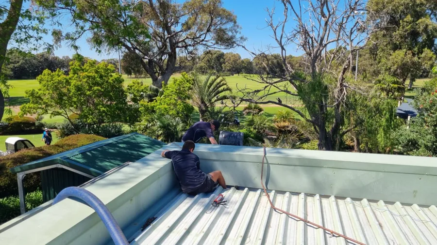 Worker clearing a commercial box gutter on a large metal roof