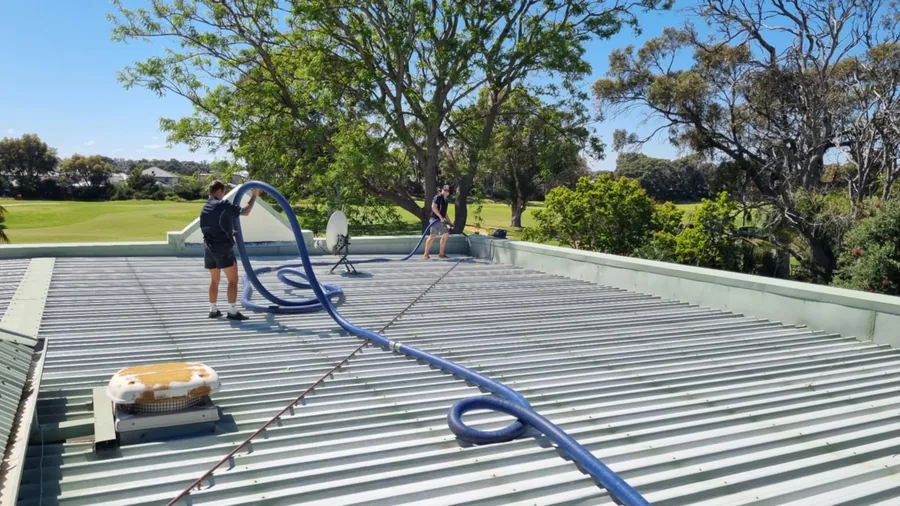 Worker vacuum cleaning a large commercial roof with a suction hose